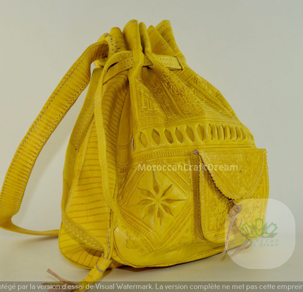 A handmade mustard yellow leather purse with intricate embossed patterns and tassel detailing.